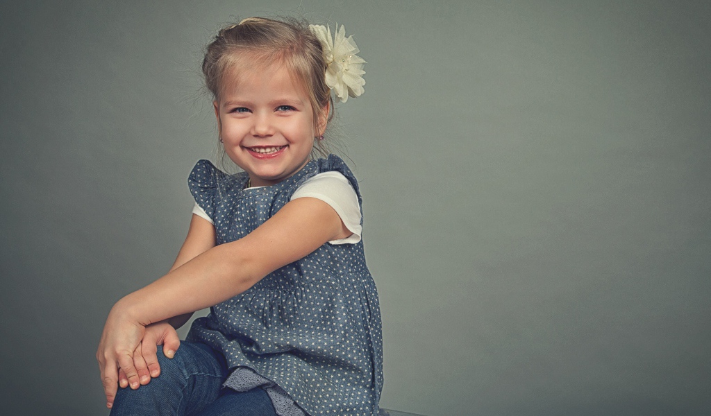 Маленькая улыбающаяся девочка с бантом на сером фоне 