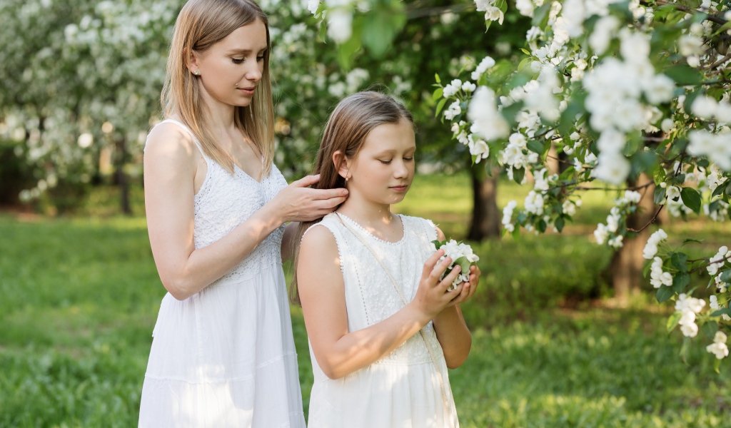 Мама заплетает дочке волосы у дерева