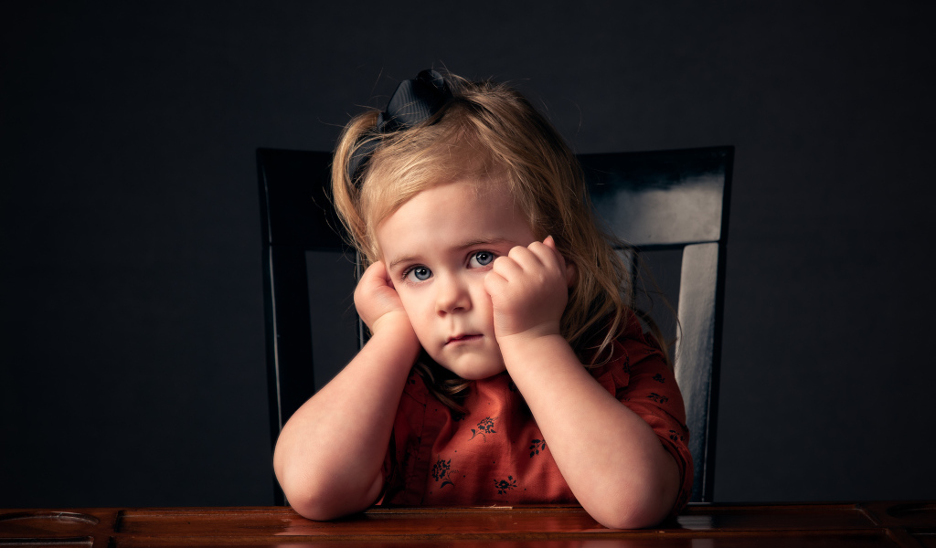 Грустная маленькая девочка сидит за столом