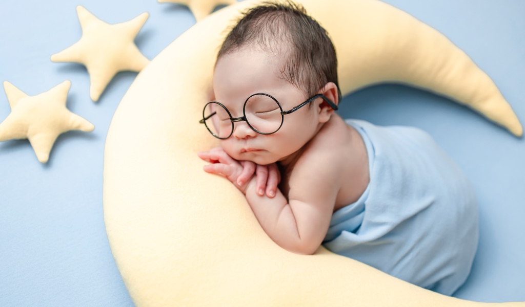 Спящий ребенок в очках на подушке в форме месяца