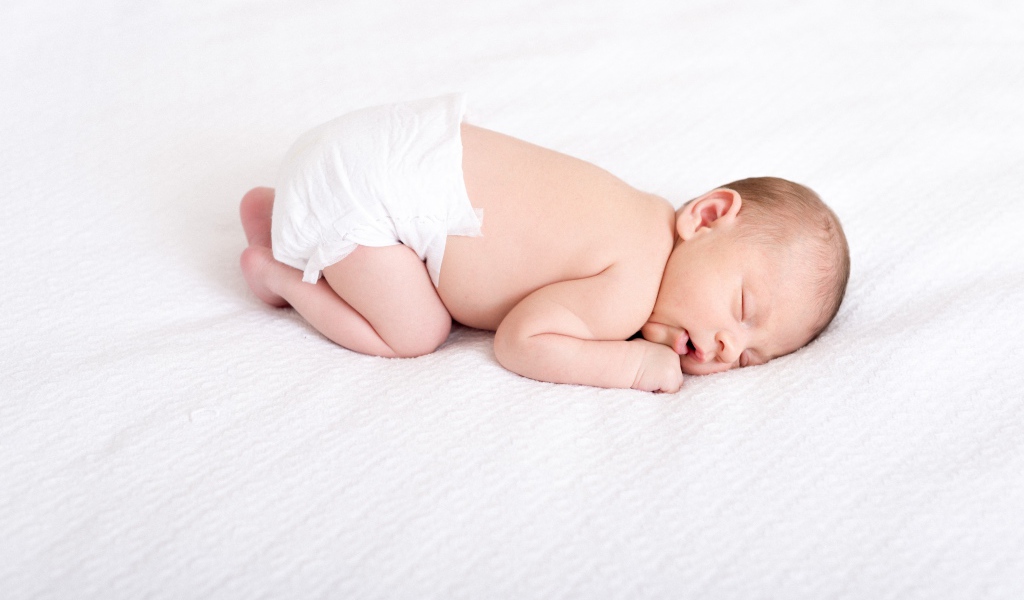 Маленький грудной ребенок в памперсе спит на белом фоне