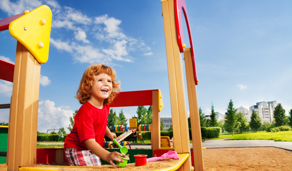 Улыбающийся мальчик в песочнице на детской площадке 