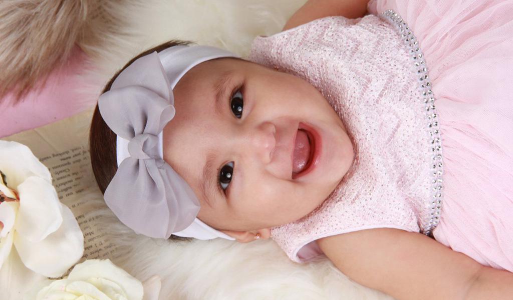 Улыбающаяся девочка в розовом платье с бантом на голове