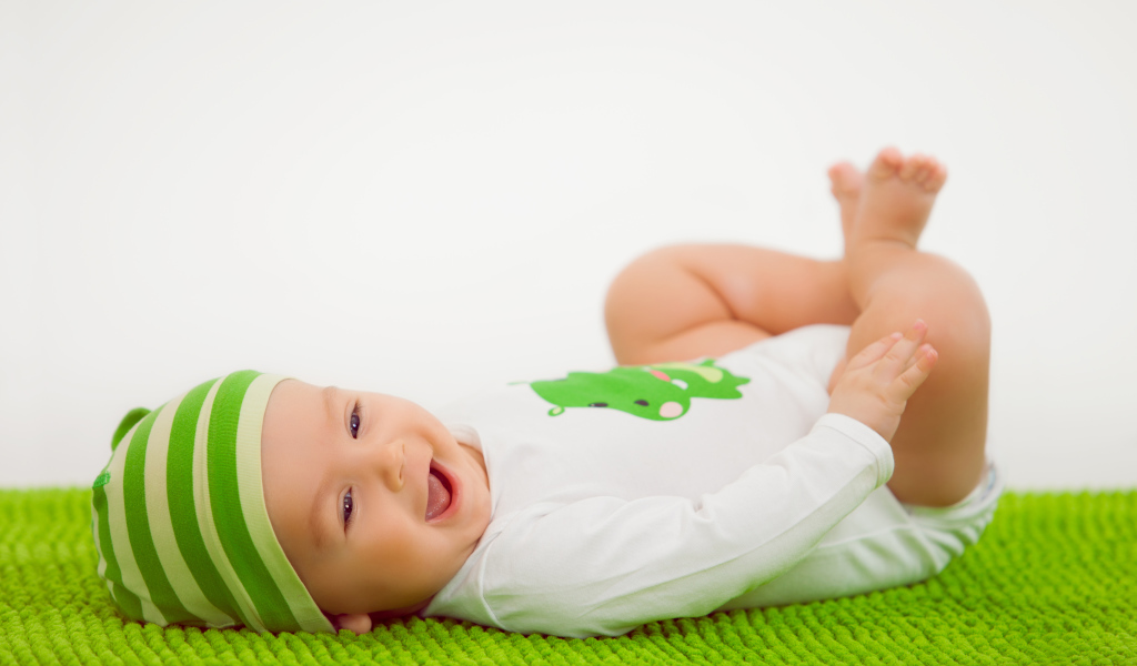 Улыбающийся маленький ребенок лежит на зеленом покрывале 