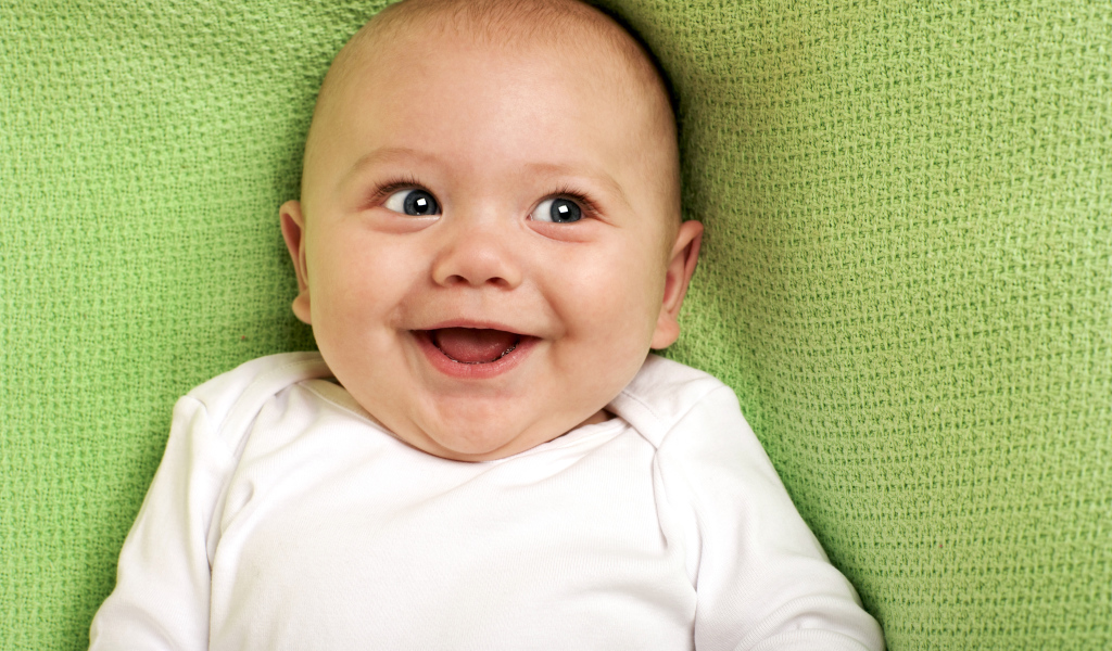 Улыбающийся маленький ребенок на зеленом покрывале 