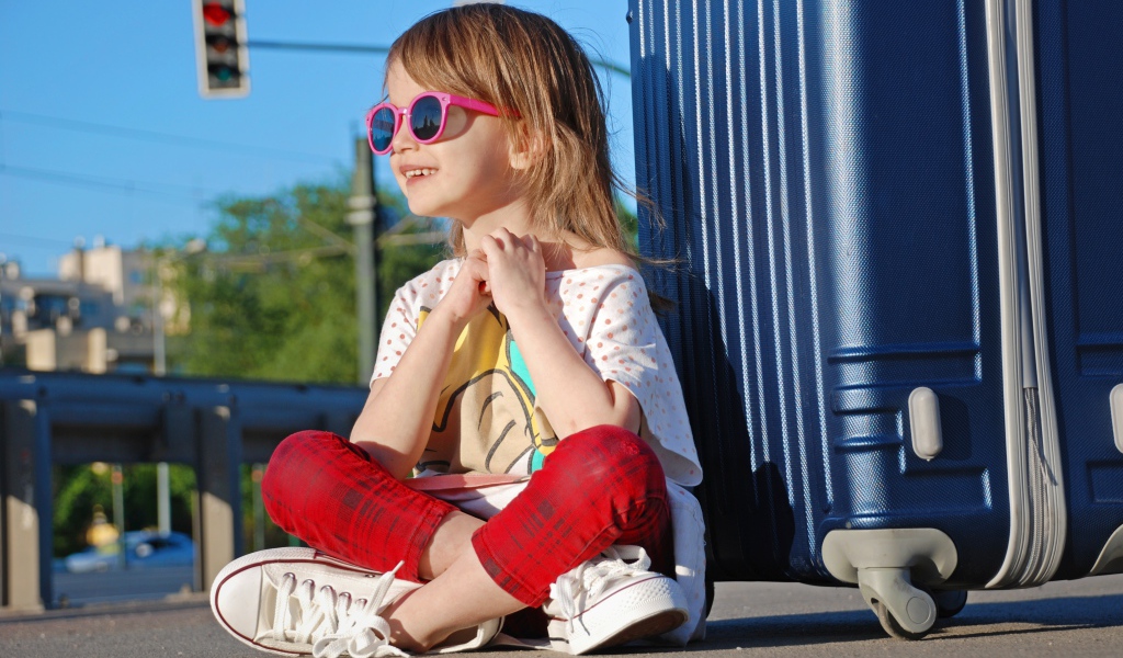 Улыбающаяся маленькая девочка в очках с чемоданом