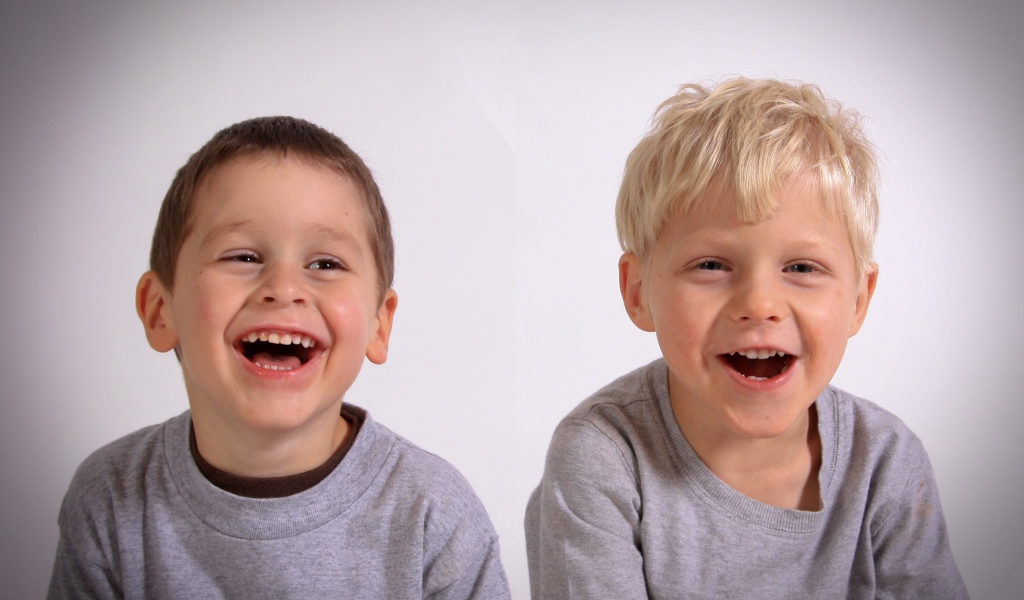 Два маленьких мальчика смеются на сером фоне