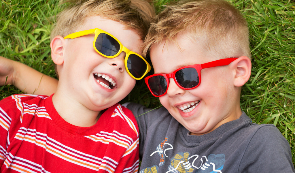 Два улыбающихся мальчика в очках на зеленой траве 