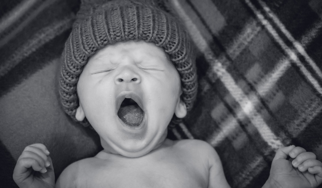 Зевающий ребенок в теплой шапке 