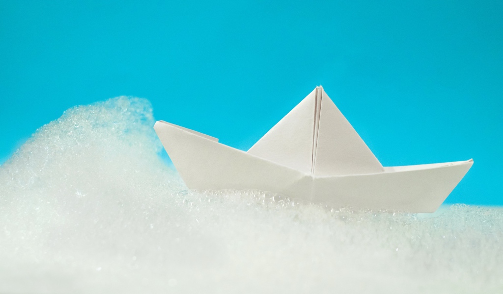 Белый бумажный кораблик на пене на голубом фоне