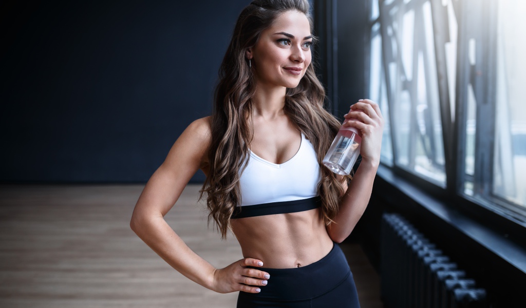 Красивая спортивная девушка с  бутылкой воды у окна