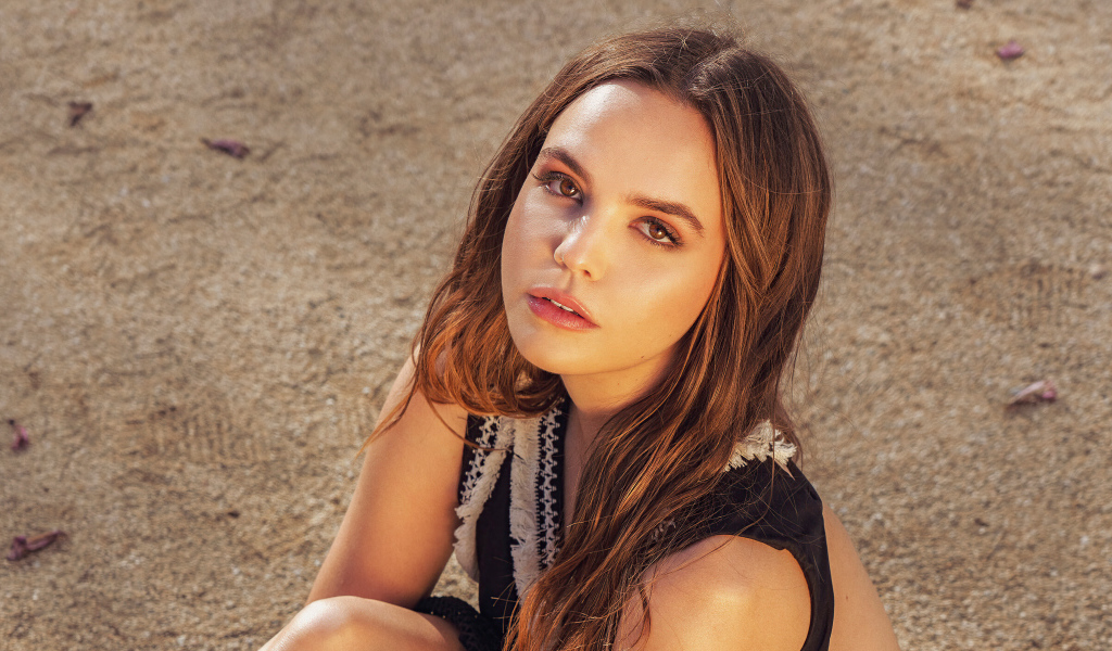 Кареглазая актриса Бэйли Мэдисон сидит на песке