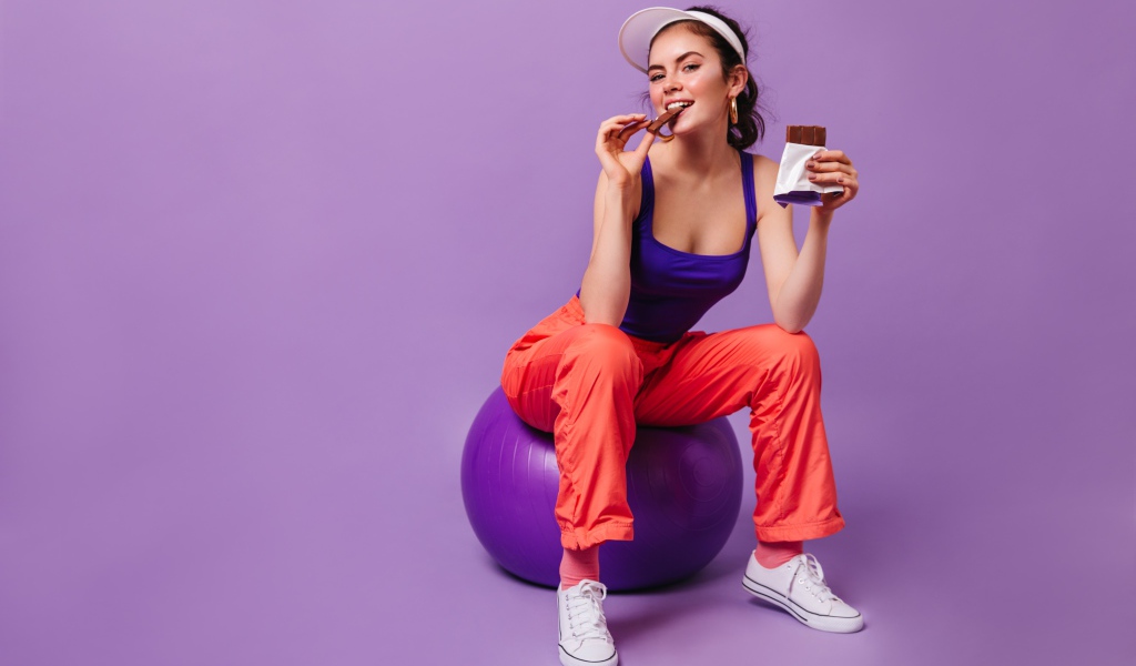 Девушка с шоколадкой сидит на фитболе