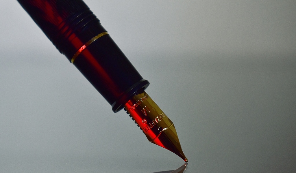 Золотое перо чернильной ручки на сером фоне