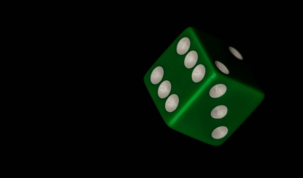 Зеленый игральный кубик на черном фоне