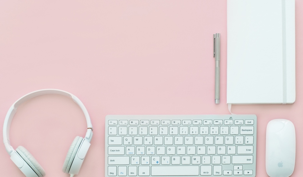 Наушники, клавиатура, блокнот с ручкой и мышка на розовом фоне