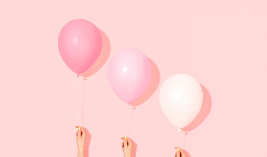 Три воздушных шарика на розовом фоне в руках