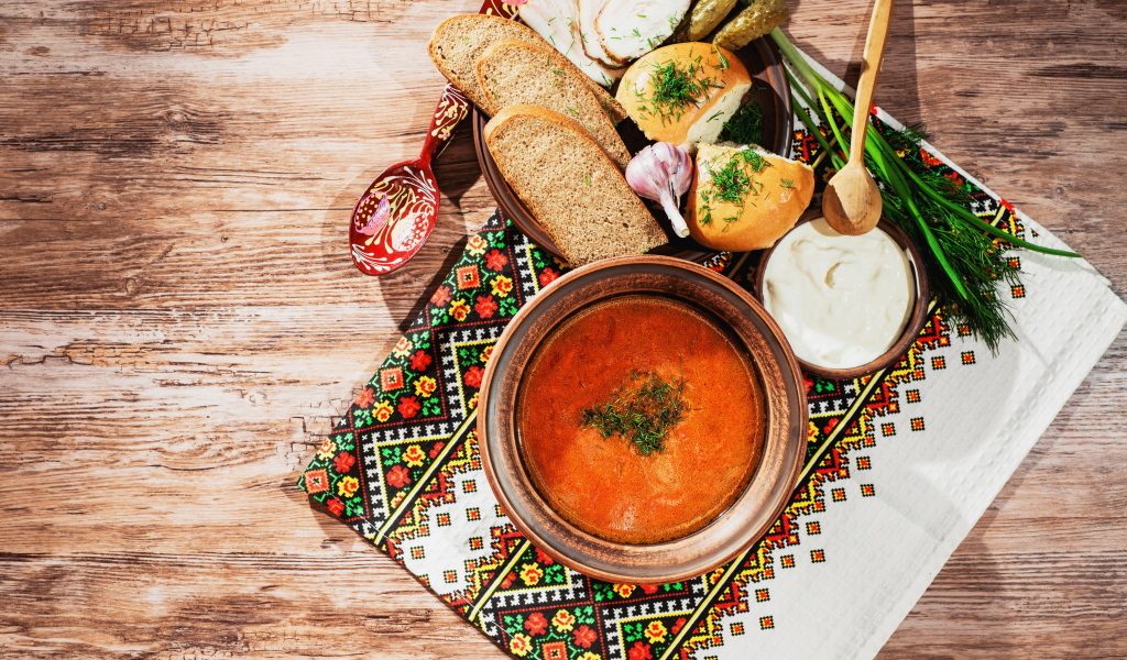 Тарелка борща на столе с салом, хлебом и зеленью