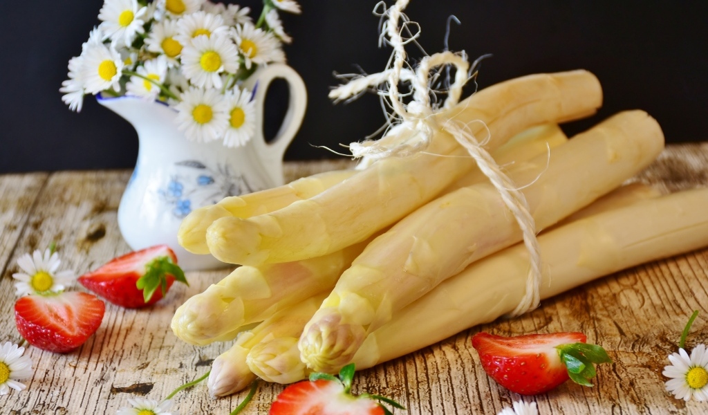 Спаржа на столе с ромашками и ягодами клубники