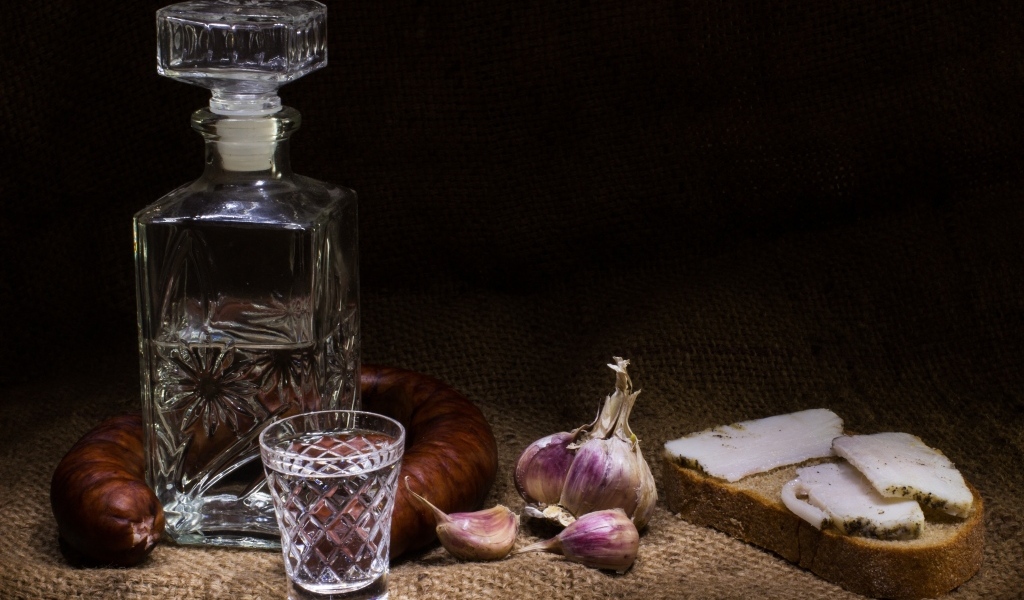 Бутылка водки на столе с салом, колбасой и чесноком