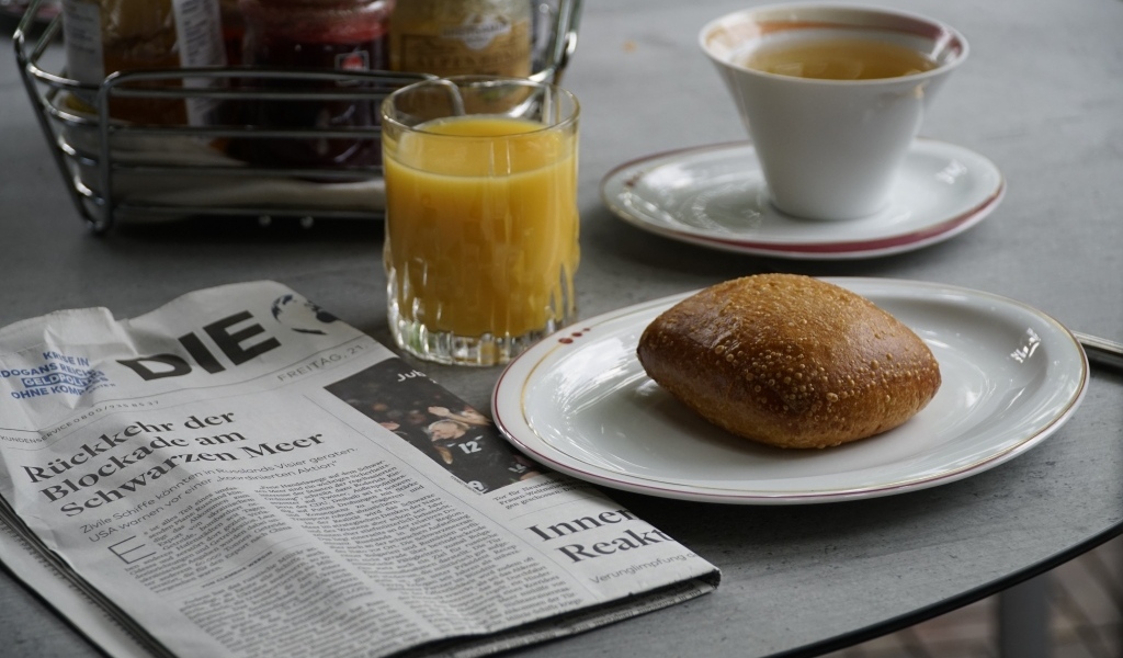 Булочка и стакан сока на столе с газетой