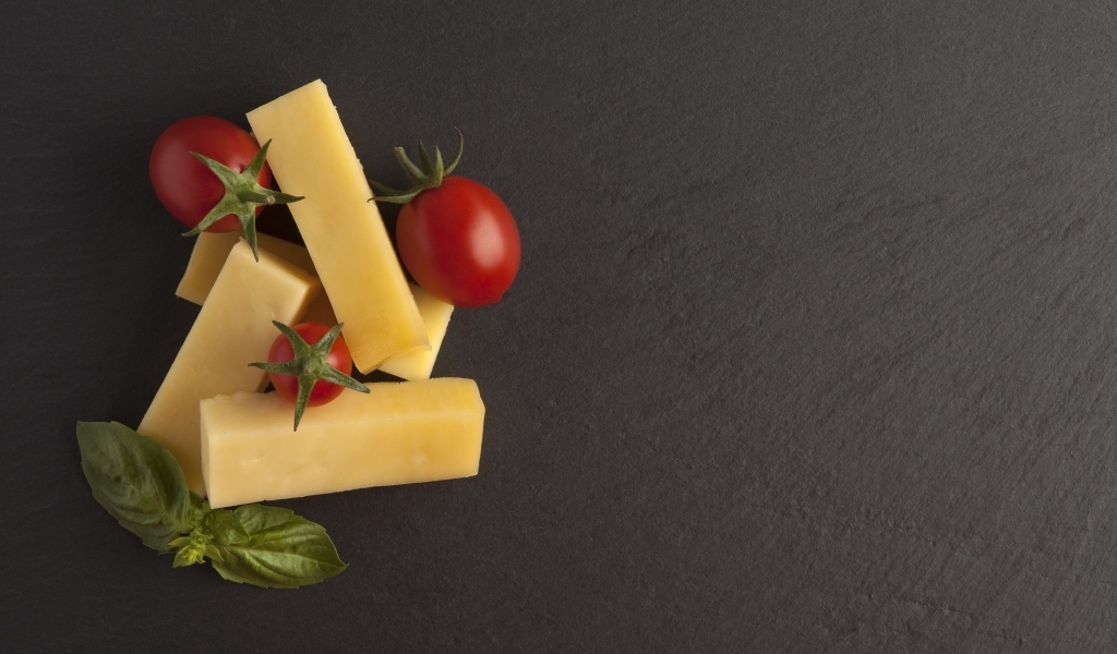 Сыр с помидорами и листьями базилика на сером столе