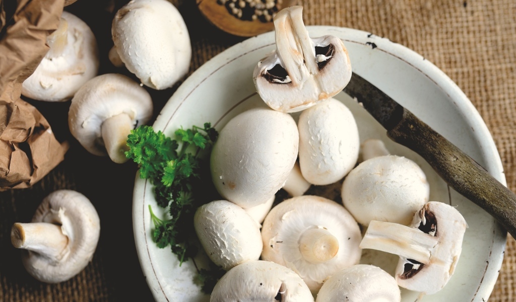 Свежие шампиньоны на тарелке на столе