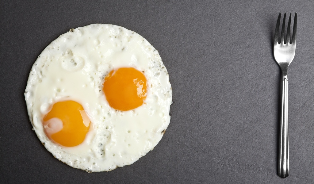 Яичница глазунья с вилкой на сером столе