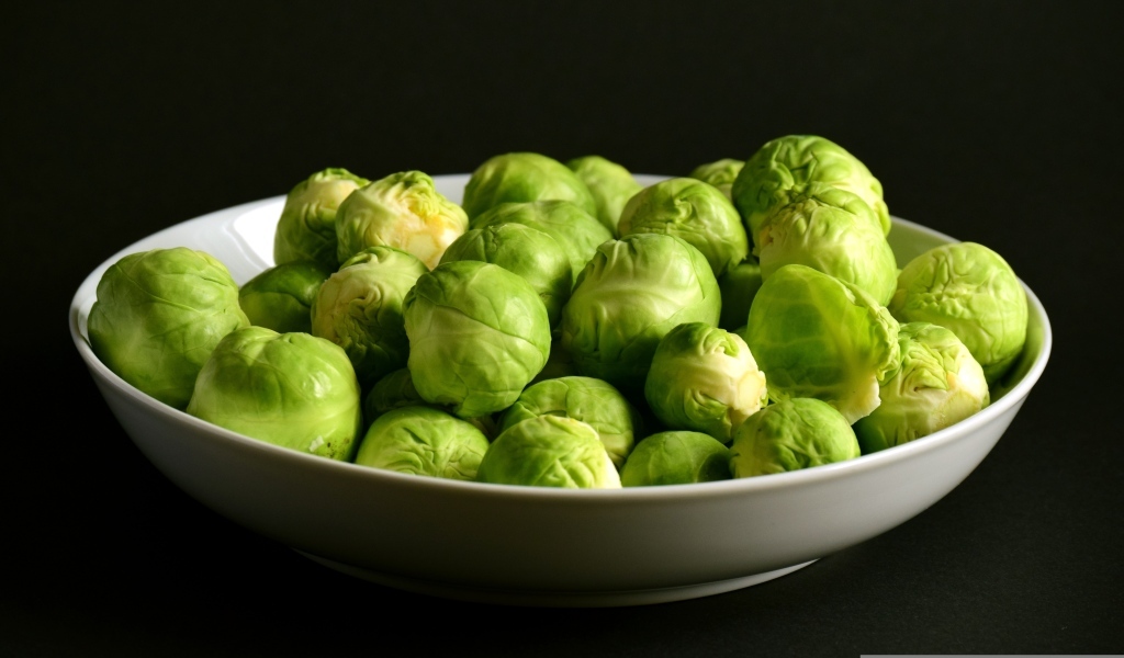 Зеленая брюссельская капуста в тарелке на черном фоне