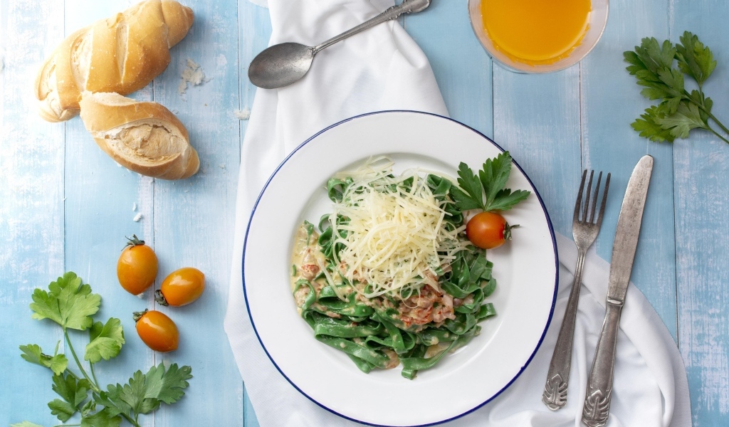 Зеленая лапша с сыром на столе с хлебом и зеленью