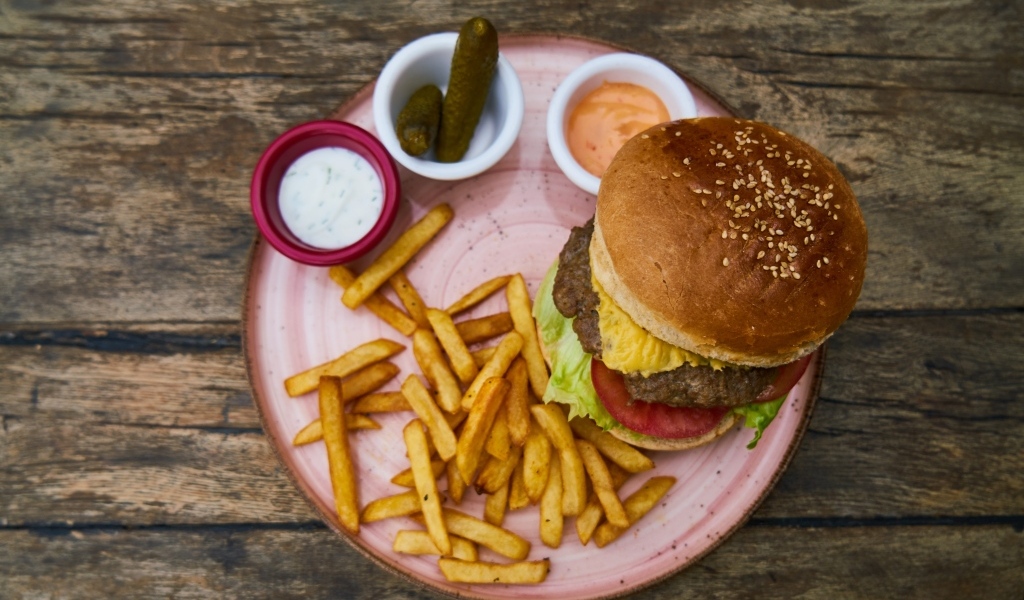 Гамбургер на тарелке с картофелем фри, огурцами и соусом