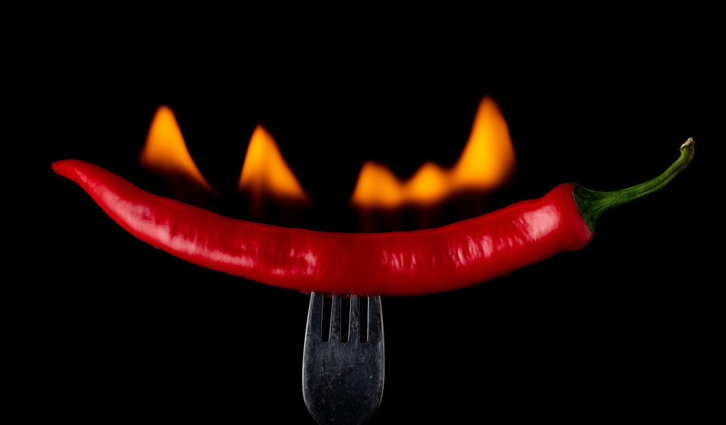 Жгучий красный перец на вилке на черном фоне