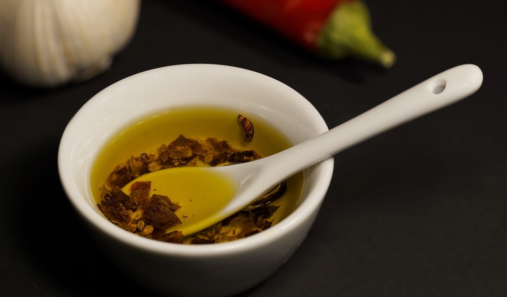 Оливковое масло в тарелке на столе с перцем и чесноком