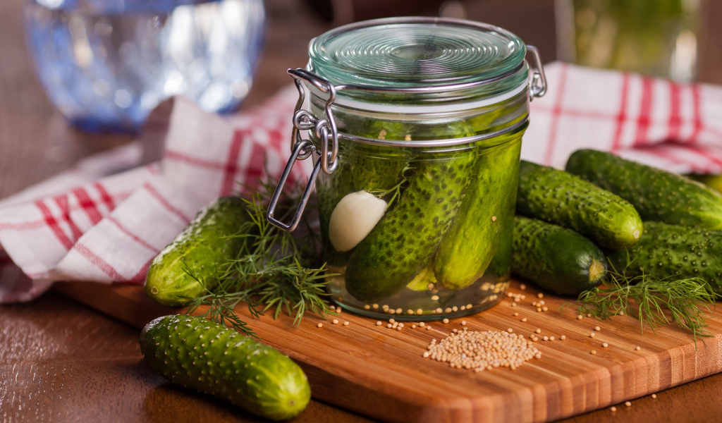 Маринованные огурцы в банке на столе со свежими