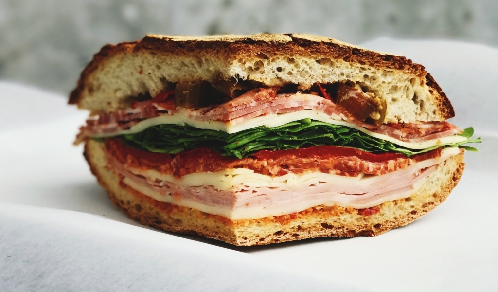 Кусок булки с колбасой, ветчиной и листьями салата