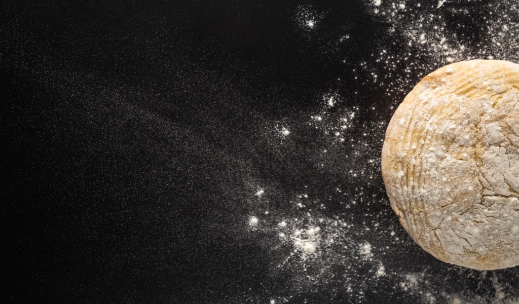 Сырое тесто на черном столе с мукой