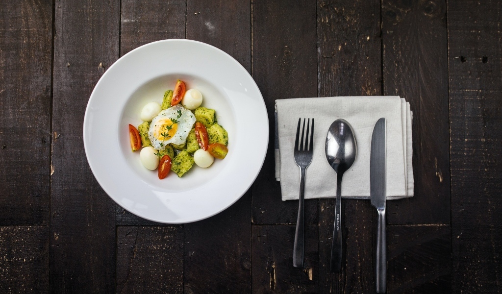 Яичница с овощами в белой тарелке на столе со столовыми приборами