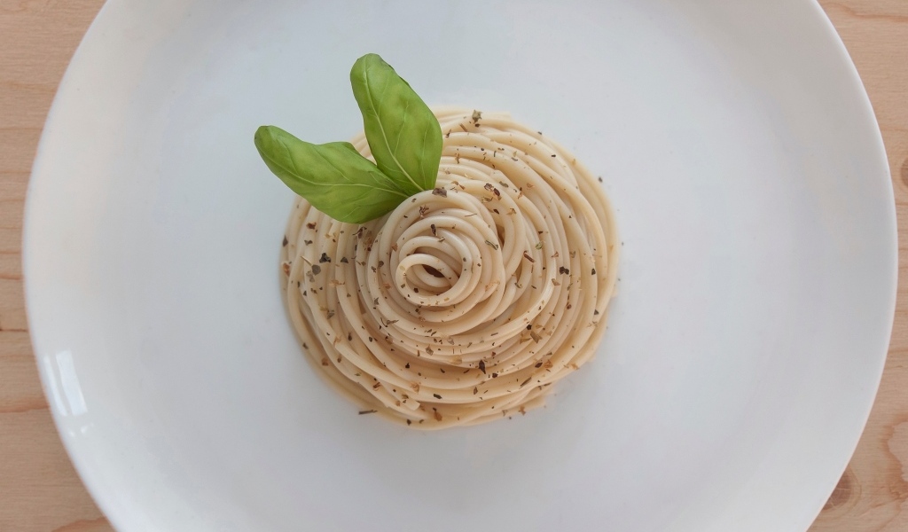 Спагетти с листьями базилика на белой тарелке