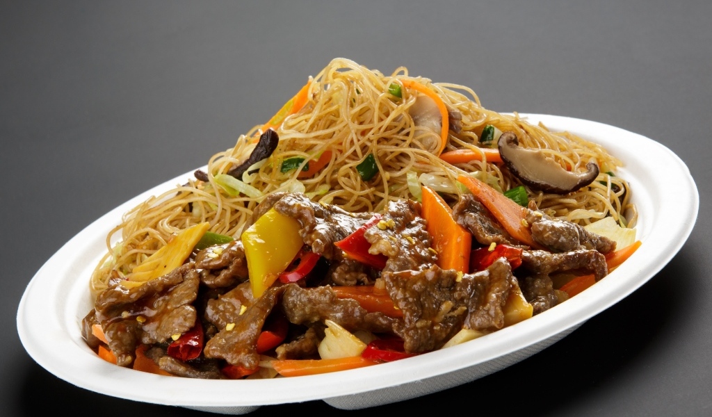 Острая лапша с грибами на белой тарелке на сером фоне