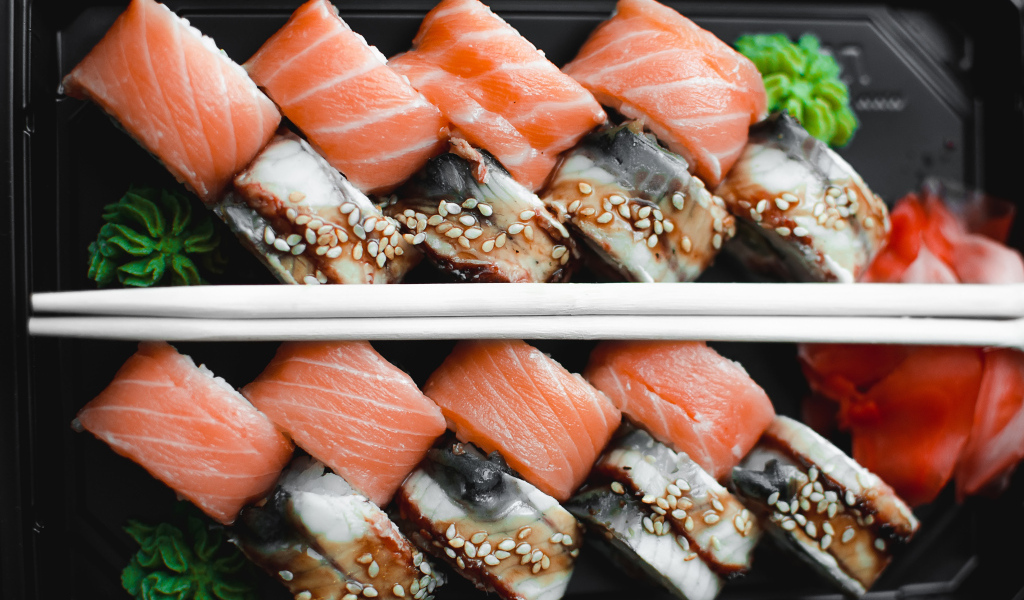 Суши с рыбой на черной тарелке с палочками