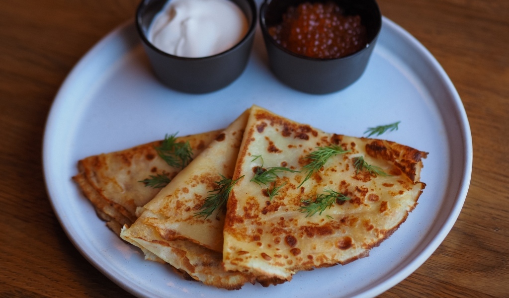 Тонкие блинчики на тарелке с красной икрой и сметаной