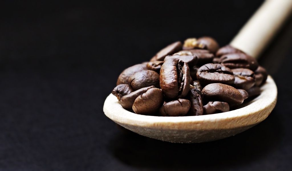 Зерна кофе на деревянной ложке на черном фоне