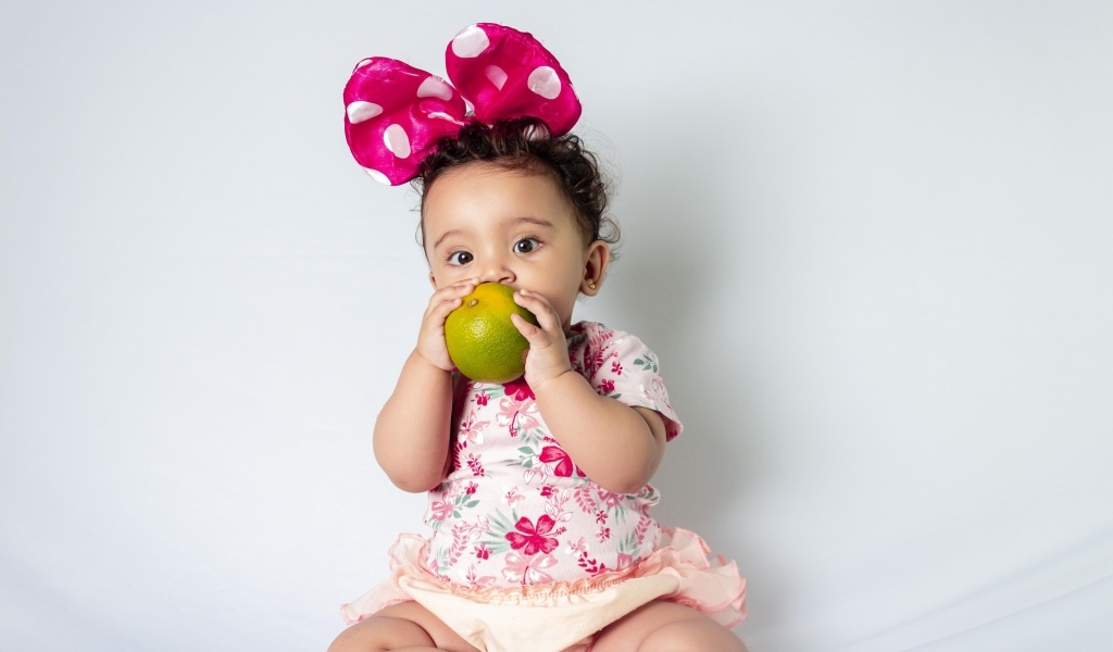 Девочка с большим бантом на голове ест апельсин