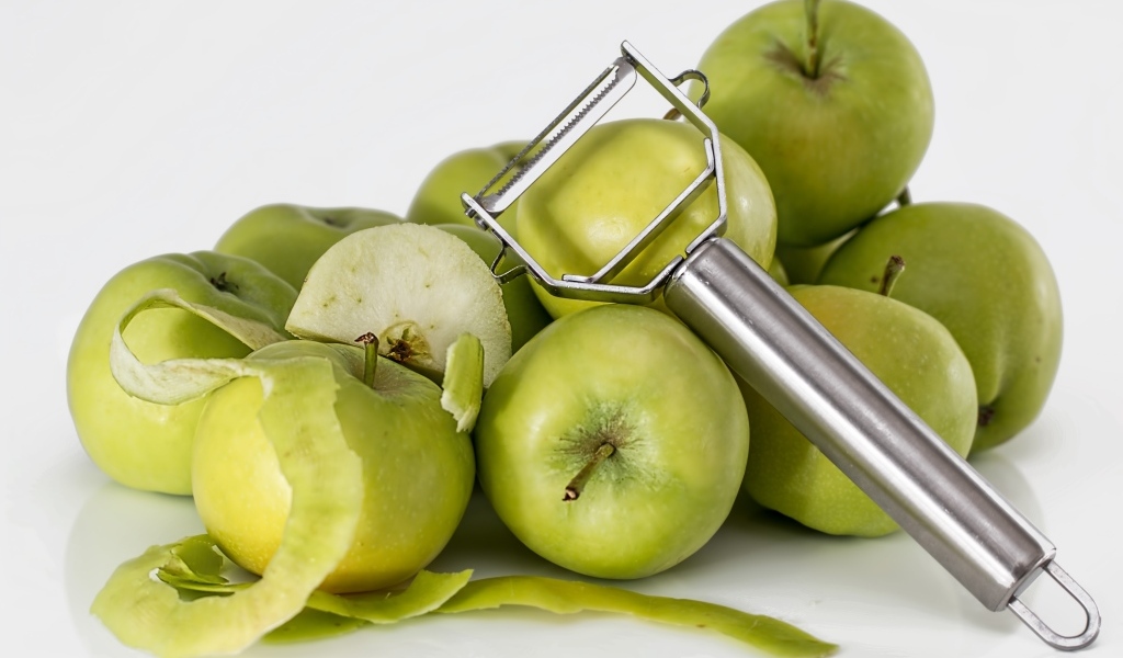 Зеленые яблоки с овощечисткой на белом фоне