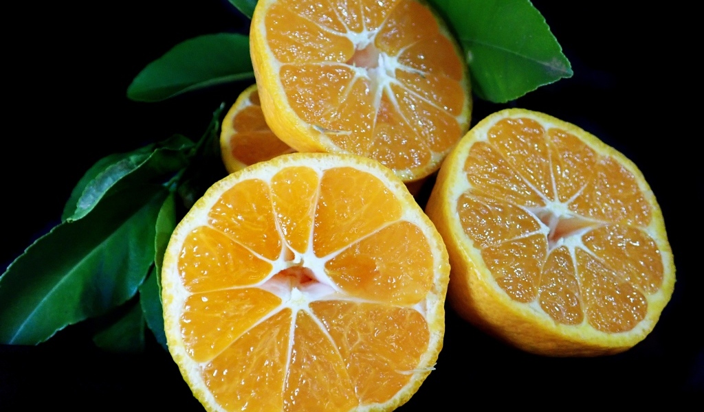Половинки мандарина с зелеными листьями на черном фоне