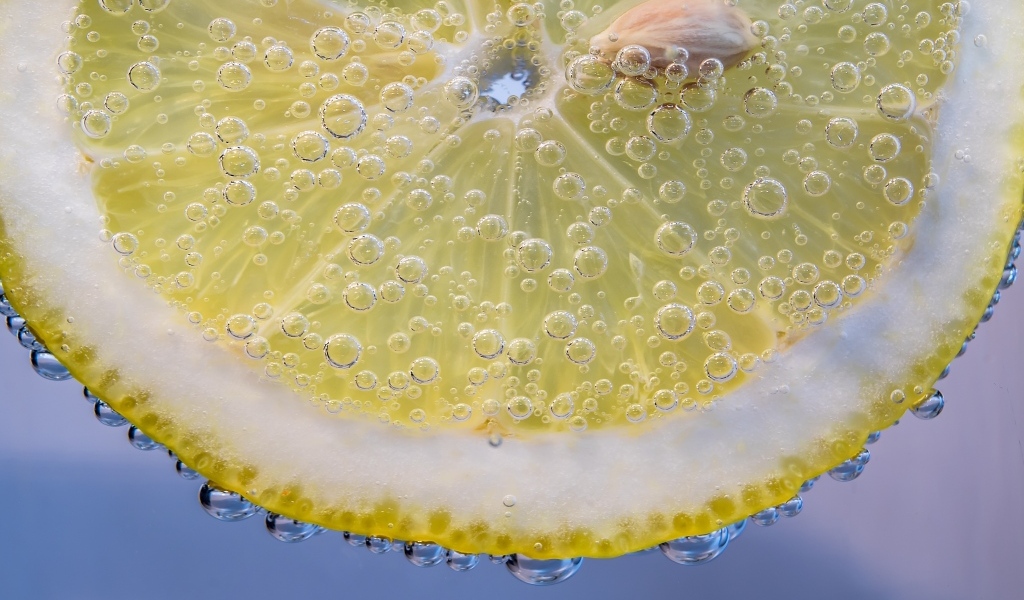 Кружок лимона в каплях воды на голубом фоне