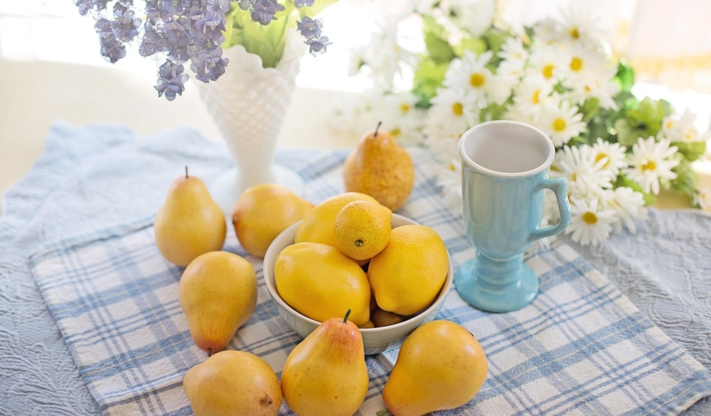 Лимоны и груши на столе с цветами