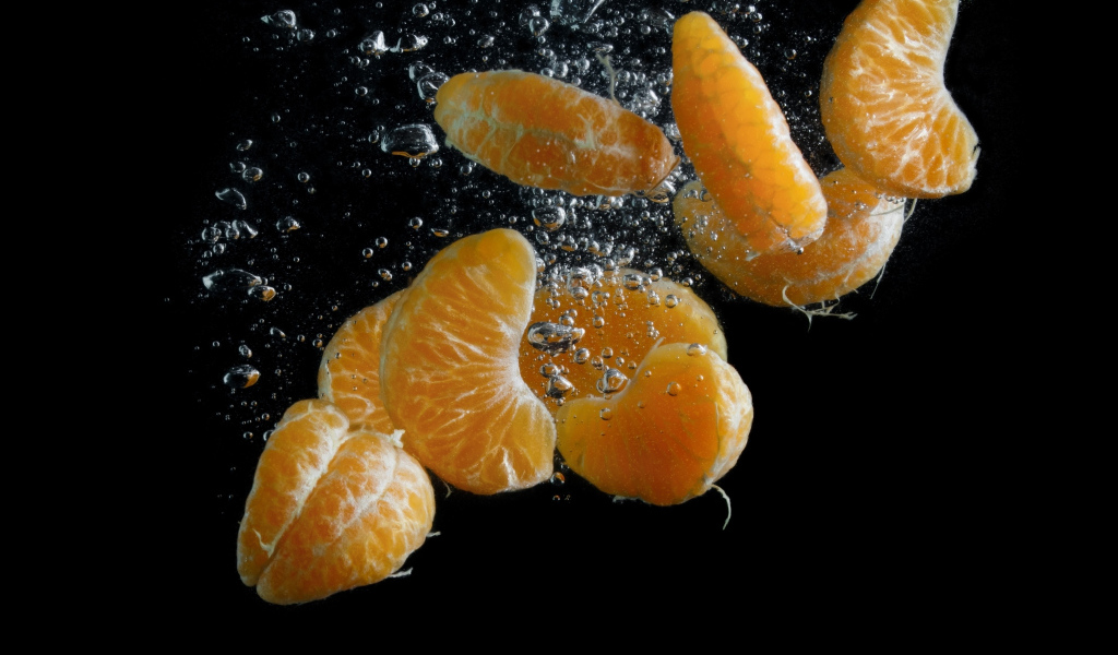 Дольки мандарина в воде на черном фоне