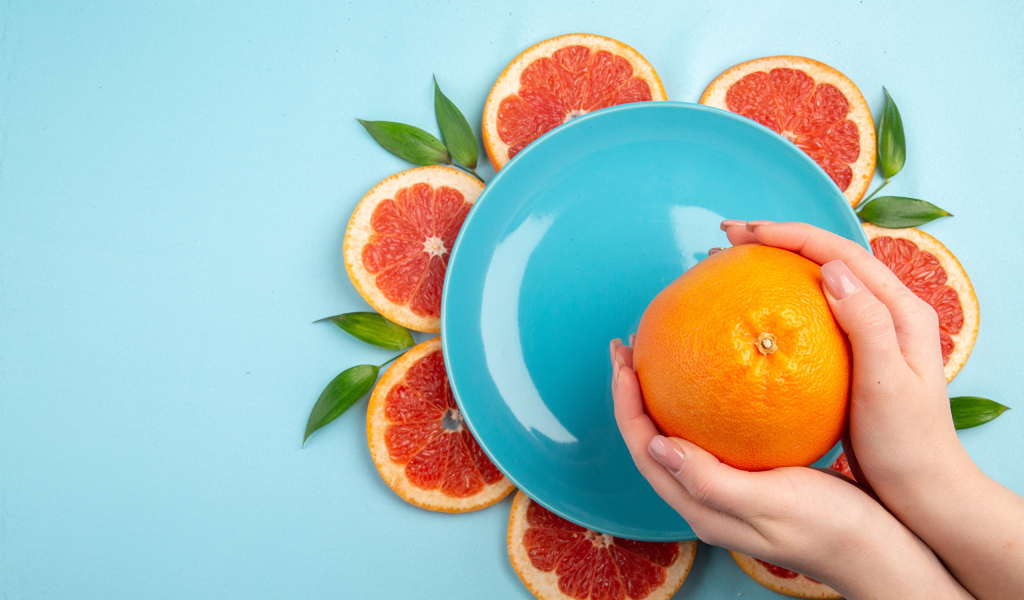 Апельсин в руках девушки на голубом фоне с тарелкой