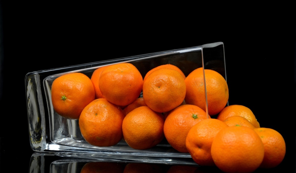 Оранжевые мандарины в стакане на черном фоне